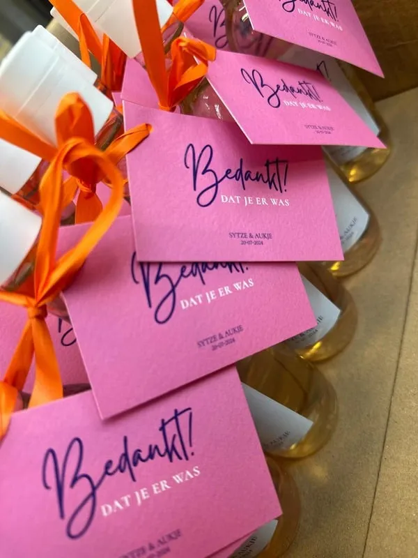 Roze bedanklabels met sierletters aan oranje linten