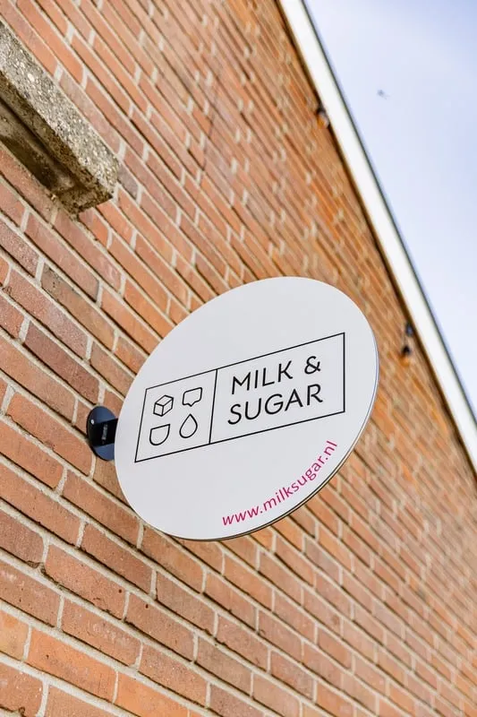 Het ovale gevelbord van Milk&Sugar aan de bakstenen muur van het pand