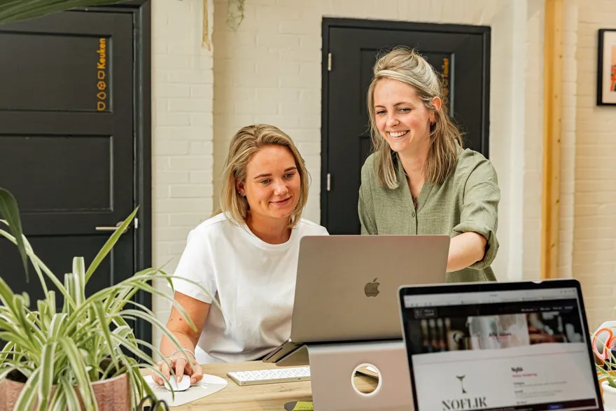 Astrid en Ruth samen achter de laptop aan de balie van de studio